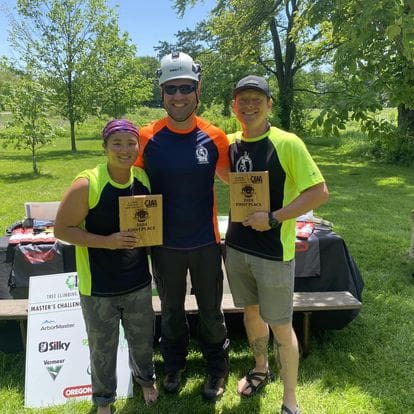 Three people holding awards for tree climbing.