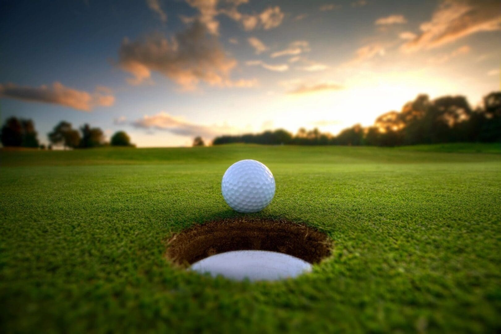 Golf ball near hole at sunset.