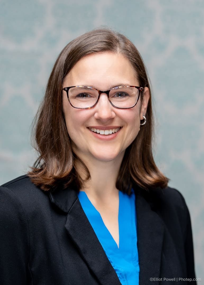 Smiling person with glasses and brown hair.