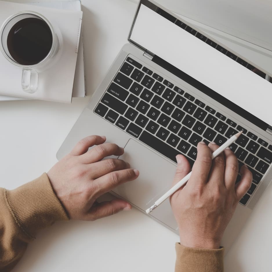 Hands typing on laptop with coffee nearby.