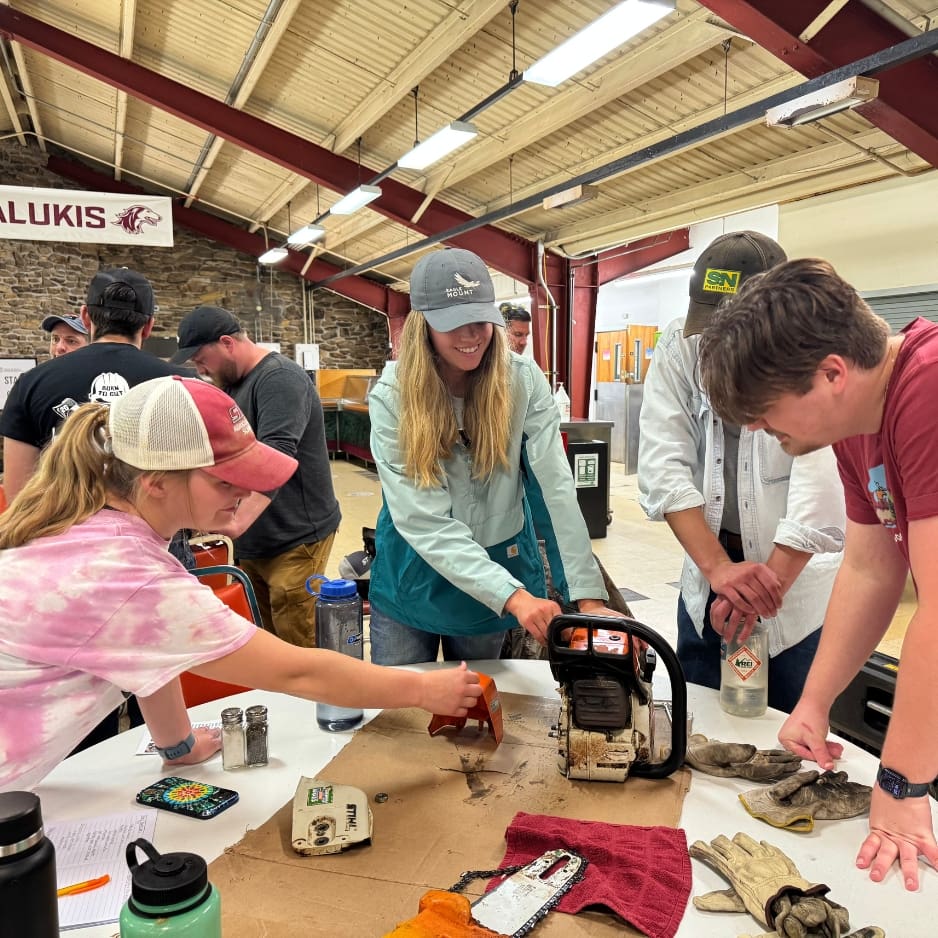 Group learning about chainsaw maintenance indoors.