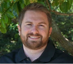 Man smiling under a tree, wearing black shirt.