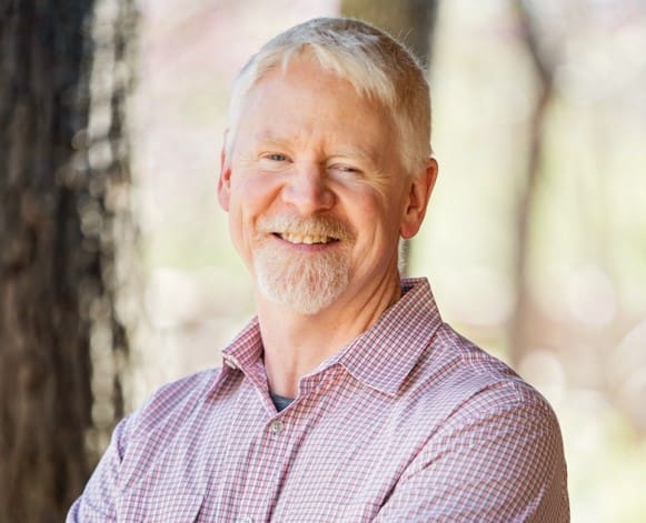 Smiling man outdoors in plaid shirt.