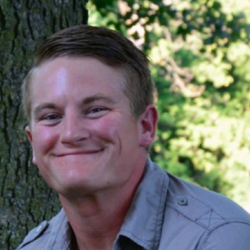 Smiling man leaning against a tree